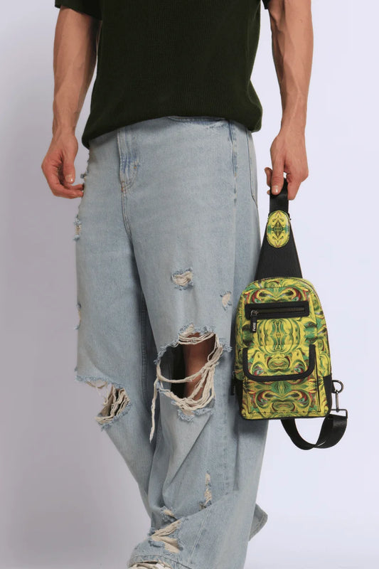 Full product view of a Person wearing ripped jeans holding a Kosmic Immersion Helios sling bag for men against a white background