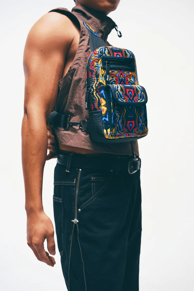 Close-up of zipper closure on a vegan leather sling bag worn by a man with a neutral background