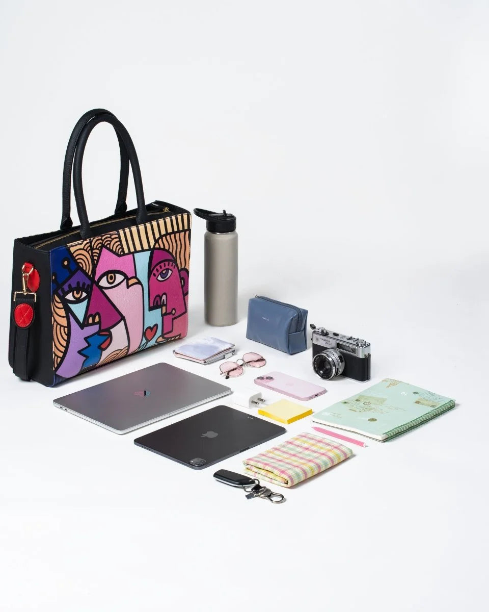 Women’s tote bag holding work essentials and notebook, a laptop, camera, and water bottle on a white background
